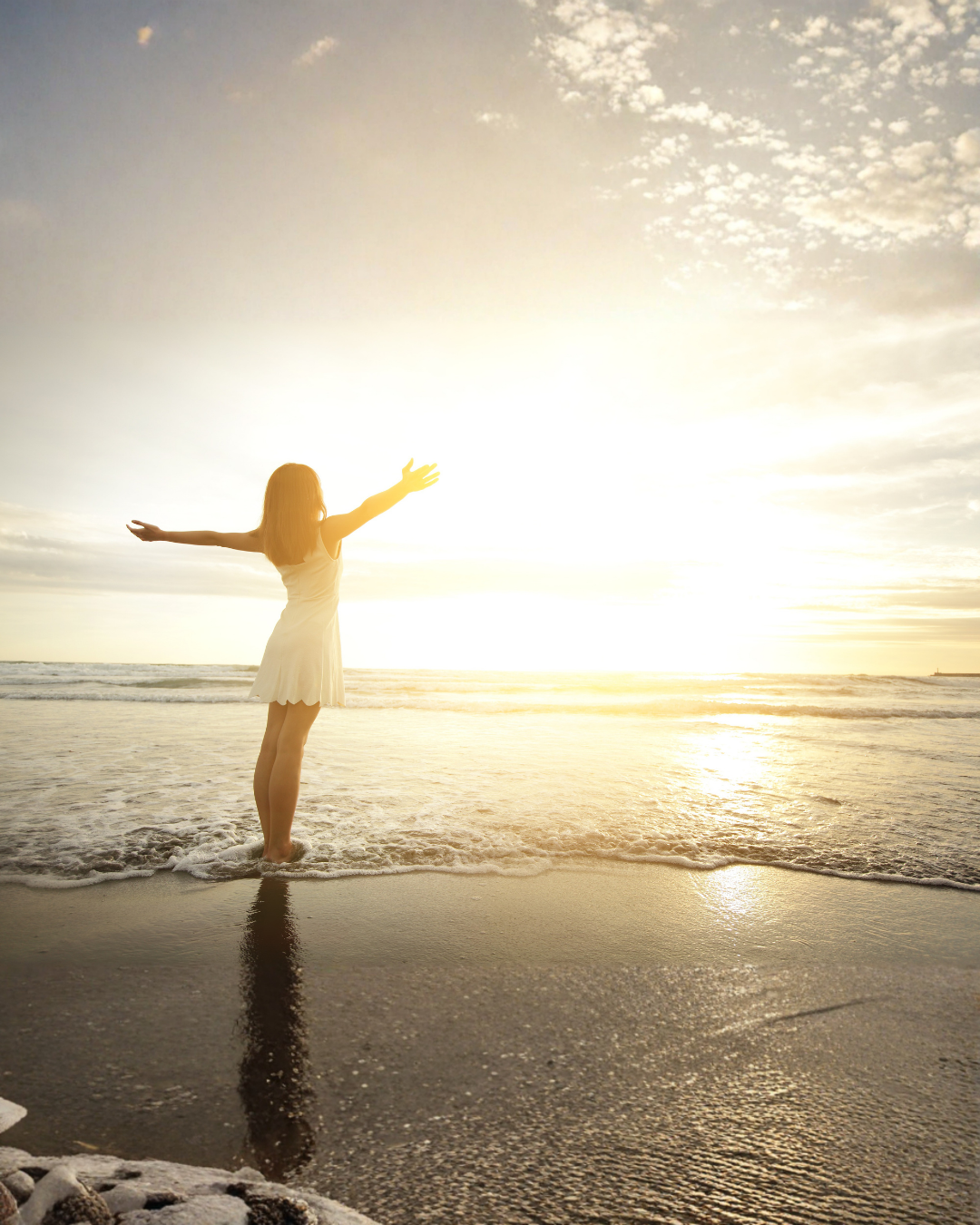 Femme les bras ouverts face au coucher de soleil sur la plage, symbole de liberté et de bien-être retrouvé