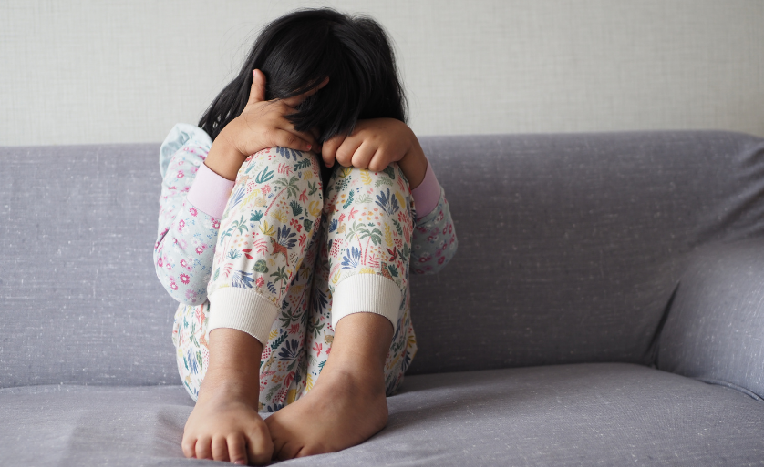 Petite fille assise sur un canapé, les bras autour des genoux et la tête baissée